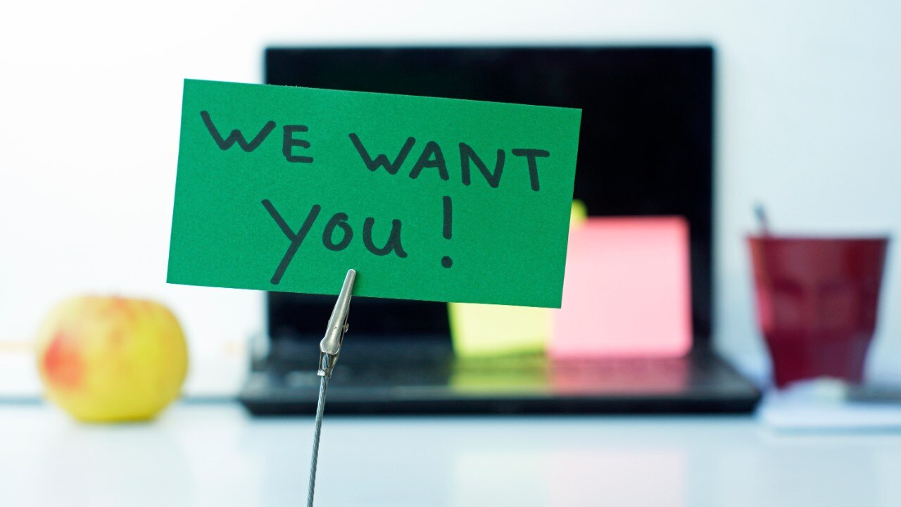 Green sign on desk that says "we want you!"