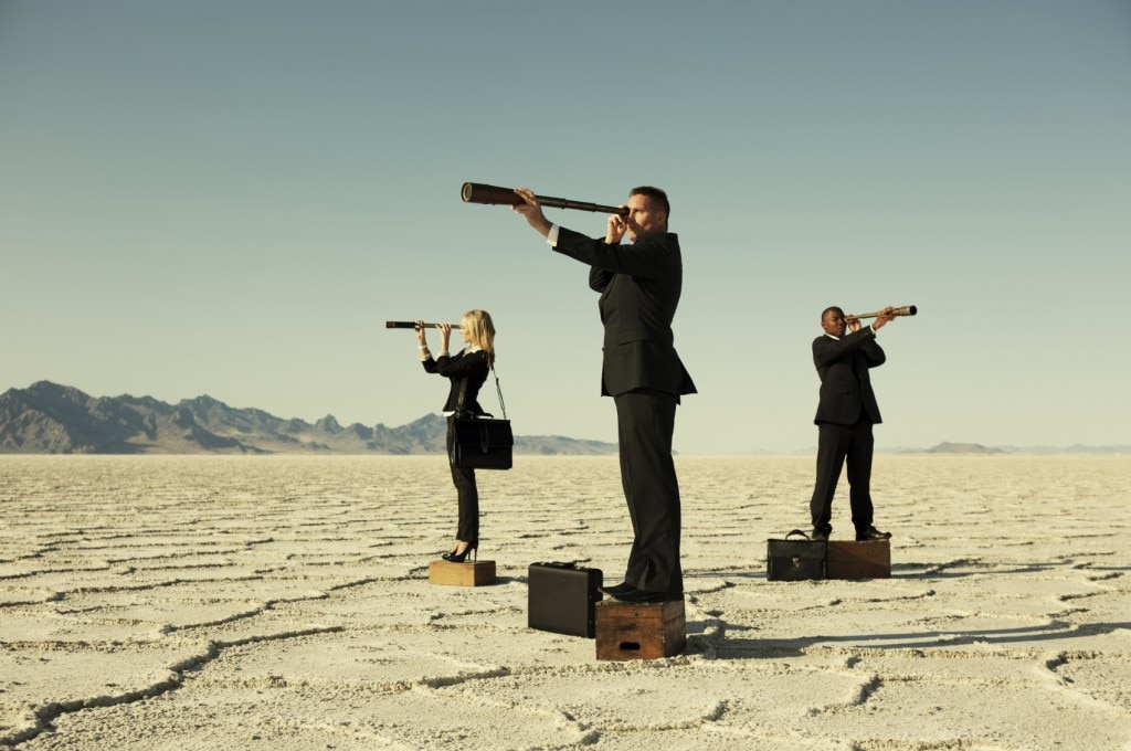 People in suits with telescopes standing on boxes in a desert