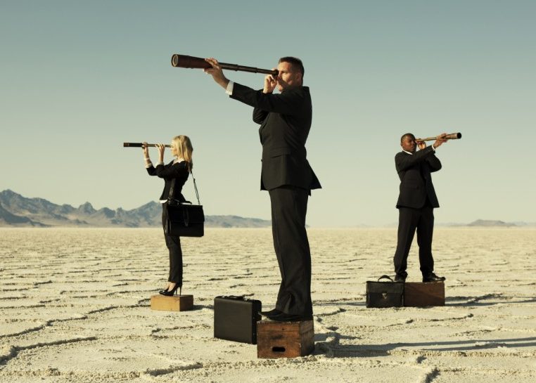 People in suits with telescopes standing on boxes in a desert