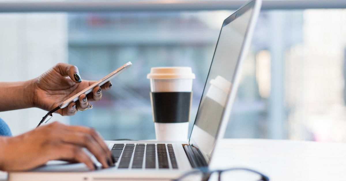 Holding a phone and typing on a MacBook in a coffee shop