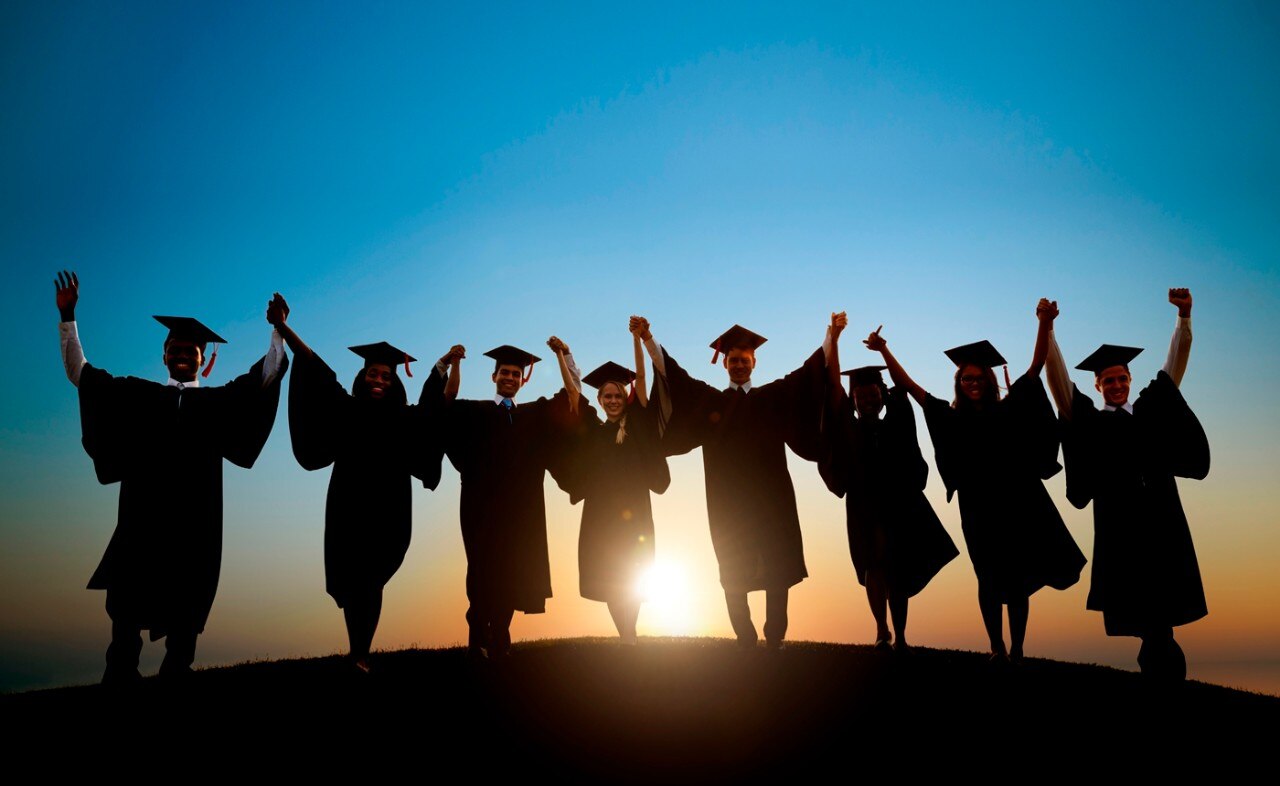 Estudiantes con gorros y batas de graduación caminando hacia la puesta de sol