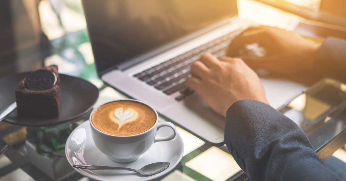Mains tapant sur un MacBook avec café et gâteau sur la table
