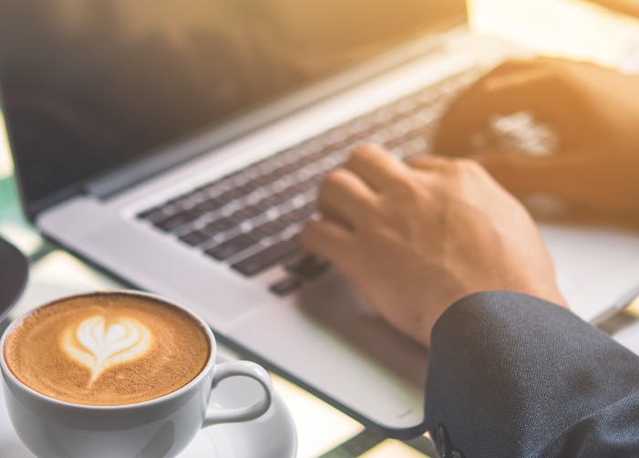 Mains tapant sur un MacBook avec café et gâteau sur la table