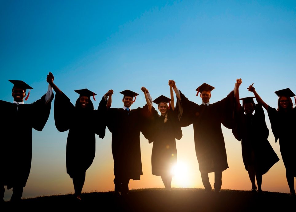 Des étudiants portant des casquettes et des blouses de remise de diplôme marchent vers le coucher du soleil