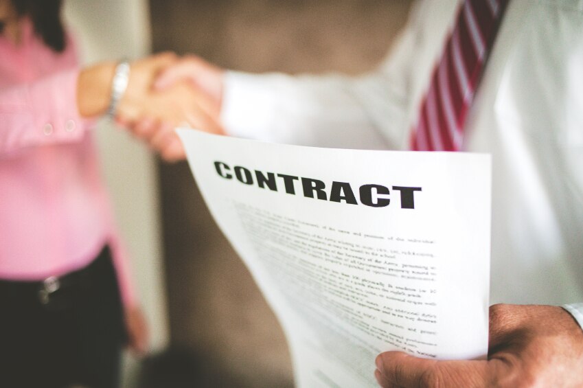 Personnes floues se serrant la main avec un papier sur lequel la mise au point est « Contrat »