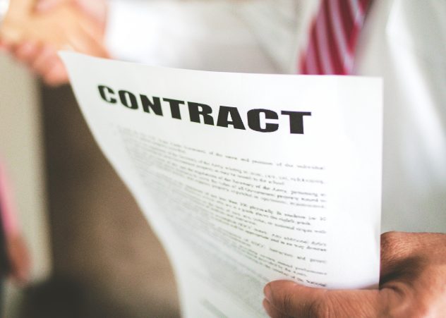 Personnes floues se serrant la main avec un papier sur lequel la mise au point est « Contrat »