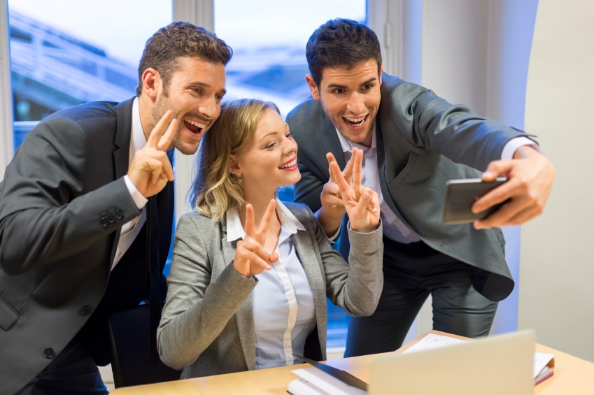 3 personnes qui font des signes de paix tout en prenant un selfie en tenue professionnelle