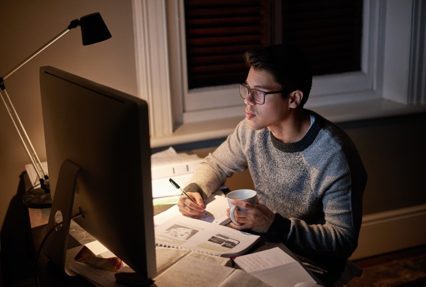 Étudiant révisant un journal tard dans la nuit sous la lueur d'un écran d'ordinateur