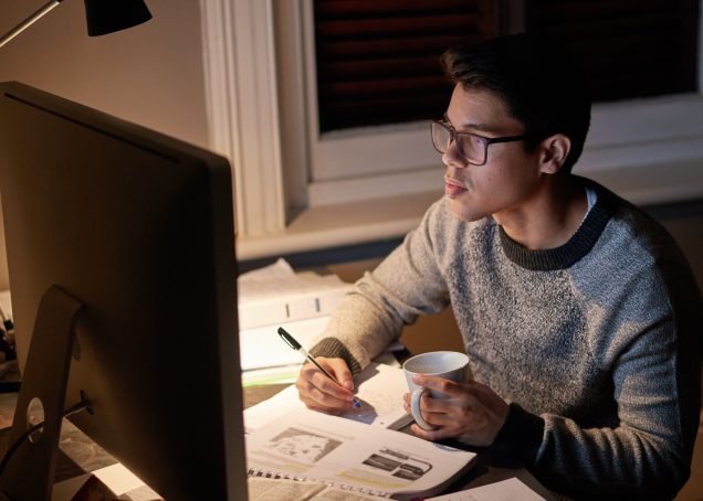 Étudiant révisant un journal tard dans la nuit sous la lueur d'un écran d'ordinateur