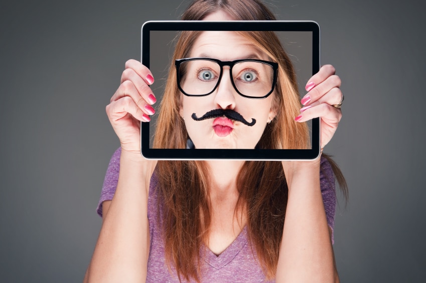 Fille tenant un iPad devant son visage avec une photo de son visage avec une fausse moustache et des lunettes
