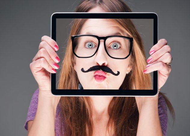 Fille tenant un iPad devant son visage avec une photo de son visage avec une fausse moustache et des lunettes