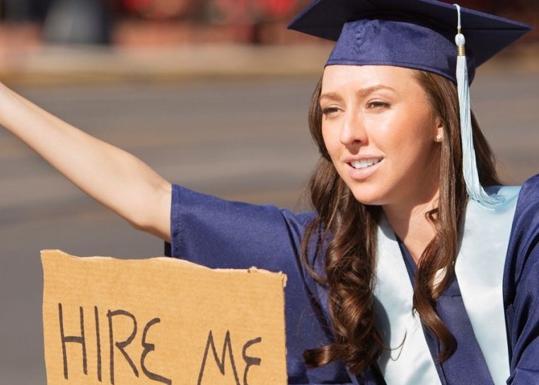 Casquette et blouse d’étudiant en remise des diplômes portant une pancarte en carton indiquant « embaucher moi »
