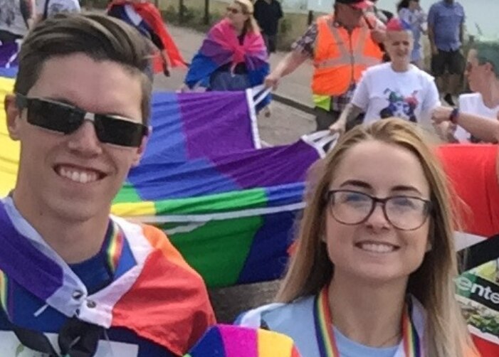 À un défilé, Luke et d’autres employés d’Enterprise arborent le grand drapeau DE FIERTÉ