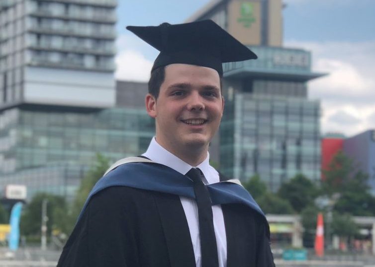 Tommy en casquette et robe de remise de diplôme devant des gratte-ciels