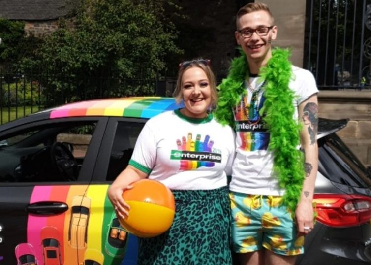 Dylan accompagné d’un autre employé d’Enterprise lors d’un événement PRIDE avec la voiture PRIDE D’Enterprise