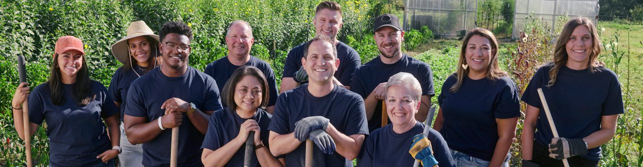 Un groupe de membres souriants de l’équipe d’Enterprise Mobility tenant des pelles et des râteaux dans un champ ensoleillé 