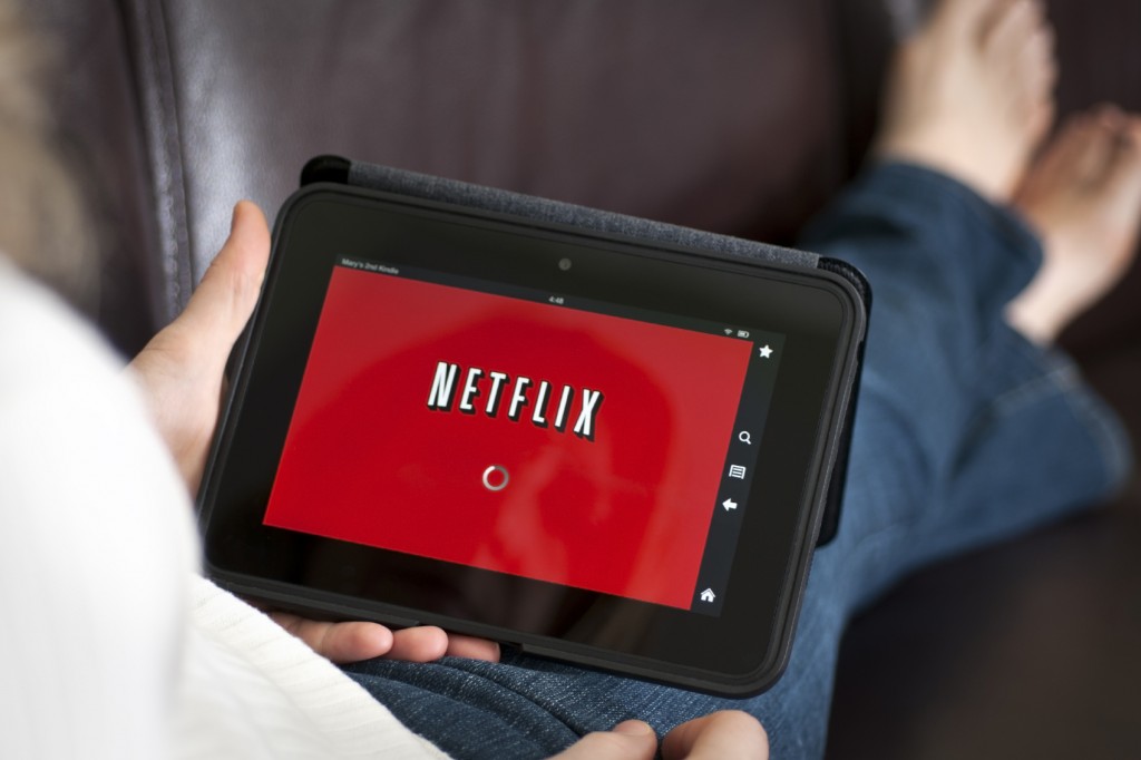 Tablette avec Netflix tenue par une personne assise sur le canapé, les jambes croisées