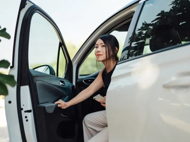 Jeune femme quittant le siège conducteur d’une minifourgonnette blanche.